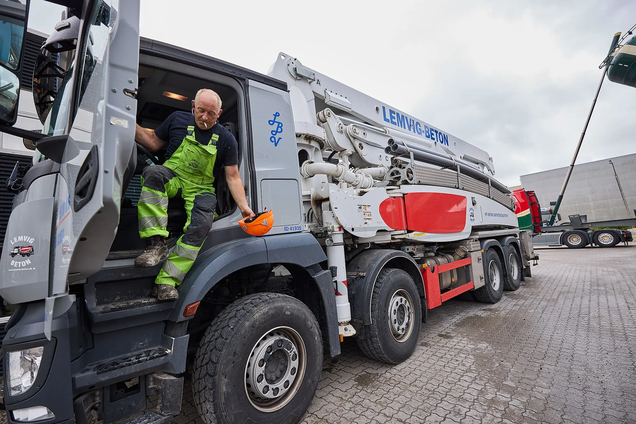 En medarbejder i grønne arbejdsbukser stiger ud af førerhuset på en hvid betonpumpebil fra Lemvig Beton.