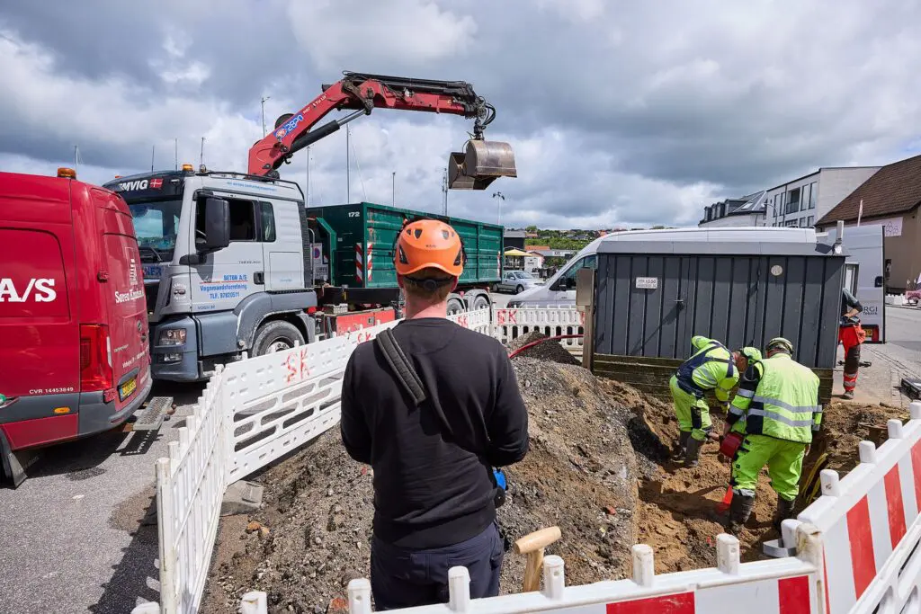 Lemvig Beton kranbil og medarbejdere i gang med gravearbejde på en byggeplads indhegnet af hvide hegn.